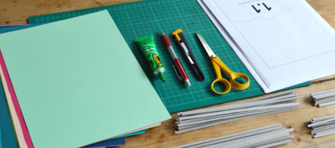 Shows the a cutting mat, scissor, pen, glue, and papers